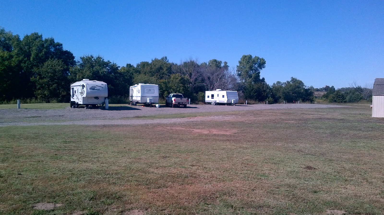 Gravel RV sites with travel trailers parked among trees at Country Horizon RV Park